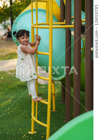 happy toddler girl playing and climbing on outdoor playground at park 126020785