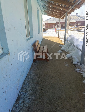 Rustic Wooden Bench in Neglected Winter Setting Against Speckled Blue Wall 126021308