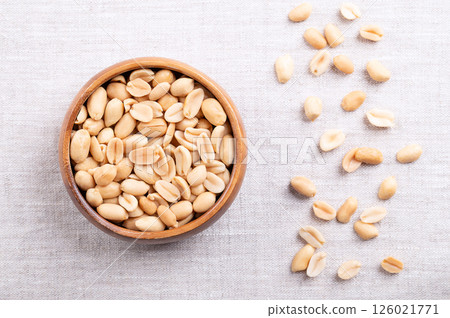 Roasted peanuts in a wooden bowl on linen fabric. Ready-to-eat crunchy snack food made from fruits of Arachis hypogaea. Light golden snack nuts with natural, nutty aroma, and firm, crunchy texture. Roasted peanuts in a wooden bowl on linen fabric. Ready-to-eat crunchy snack food made from fruits of Arachis hypogaea. Light golden snack nuts with natural, nutty aroma, and firm, crunchy texture. 126021771