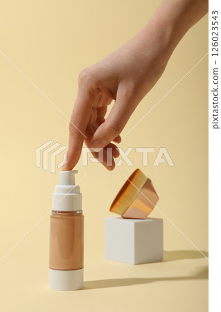 Bottle of foundation, cosmetic brush and female hand on beige background 126023543