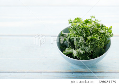 Fresh green Kale leaf salad vegetable in ceramic bowl on blue wooden background. 126024179