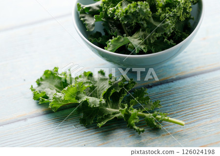 Fresh green Kale leaf salad vegetable in ceramic bowl on blue wooden background. Fresh green Kale leaf salad vegetable in ceramic bowl on blue wooden background. 126024198