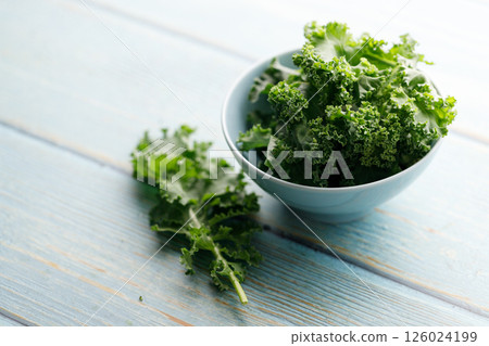 Fresh green Kale leaf salad vegetable in ceramic bowl on blue wooden background. Fresh green Kale leaf salad vegetable in ceramic bowl on blue wooden background. 126024199