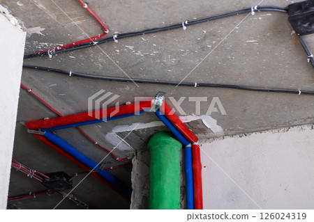 A vibrant green pipe stands surrounded by various red and blue wires 126024319