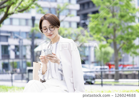 Business woman sitting on a bench and looking at her smartphone 126024688