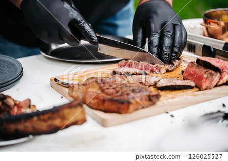 Chef slicing juicy grilled steak on wooden cutting board. 126025527
