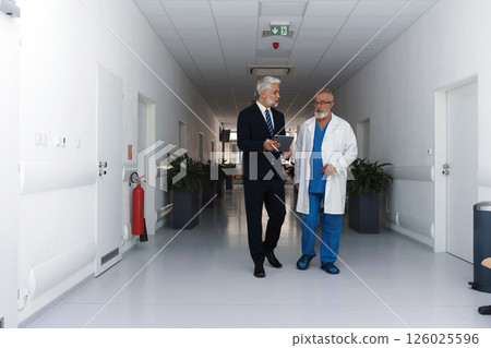 Doctor talking with hospital manager, walking down hospital hallway. Doctor talking with hospital manager, walking down hospital hallway. 126025596