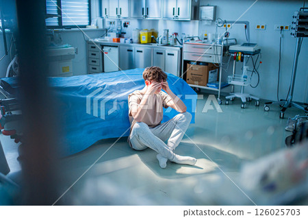 Worried teenage patient sitting alone on hospital floor, struggling with mental health issues. Worried teenage patient sitting alone on hospital floor, struggling with mental health issues. 126025703