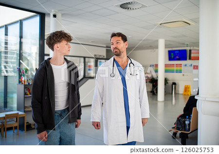 Doctor walking with teenage patient down the hospital hallway. 126025753