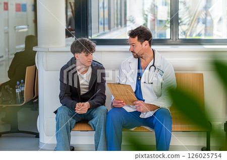 Doctor talking with teenage patient in hospital waiting room. 126025754