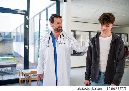 Doctor walking with teenage patient after successful medical procedure in hospital. 126025755