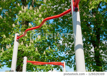 Curved outdoor horizontal bar for pull-ups in park with green trees and blue sky 126026389