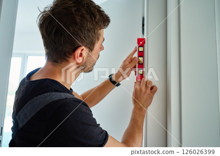 Carpenter Checking Door Alignment with Spirit Level 126026399