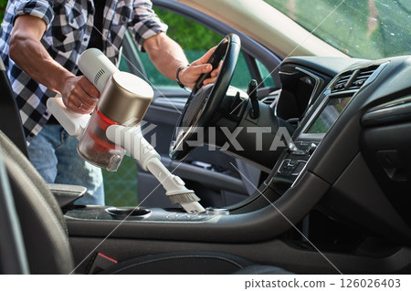 Man cleaning car dashboard with handheld vacuum cleaner 126026403