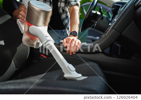 Man cleaning car dashboard with handheld vacuum cleaner 126026404