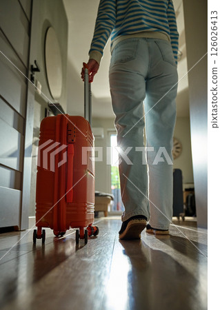 Woman rolls suitcase down hallway in apartment. Departure moment Woman rolls suitcase down hallway in apartment. Departure moment 126026413