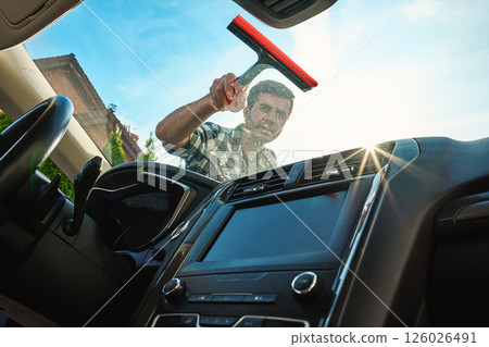 Man cleaning car windshield with squeegee from outside Man cleaning car windshield with squeegee from outside 126026491