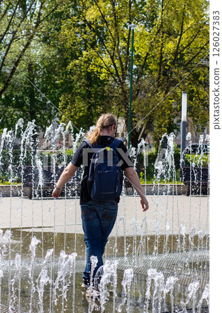 A man carrying a backpack is leisurely walking through a beautiful fountain 126027383