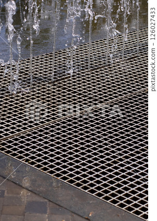 This is a closeup view of a metal grate with water flowing out from it This is a closeup view of a metal grate with water flowing out from it 126027433
