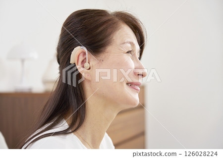 Senior woman wearing a hearing aid in living room Senior woman wearing a hearing aid in living room 126028224