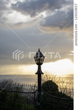 Garden lamp on a pillar. Beautiful bright lamp on a background of sunset Garden lamp on a pillar. Beautiful bright lamp on a background of sunset 126028657