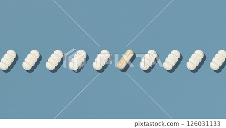 Beige medical pills in a line with one capsule on blue topview, hard light. Healthcare products Beige medical pills in a line with one capsule on blue topview, hard light. Healthcare products 126031133