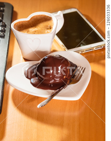 Cup of coffee and chocolate cake next to computer. 126033336