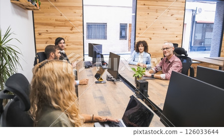 Mature businessman looking at colleagues while sitting at computer desks in office Mature businessman looking at colleagues while sitting at computer desks in office 126033644