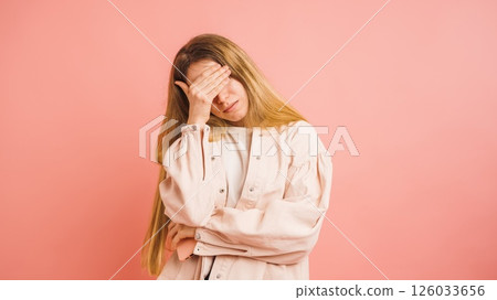 Young woman covering her eyes expressing disappointment on pink background Young woman covering her eyes expressing disappointment on pink background 126033656
