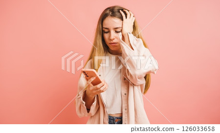 Stressed young woman reading bad news on smartphone on pink background Stressed young woman reading bad news on smartphone on pink background 126033658