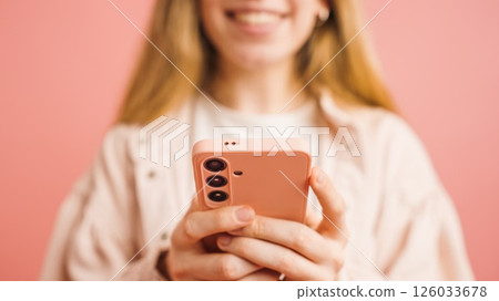 Woman smiling and using smartphone on pink background 126033678