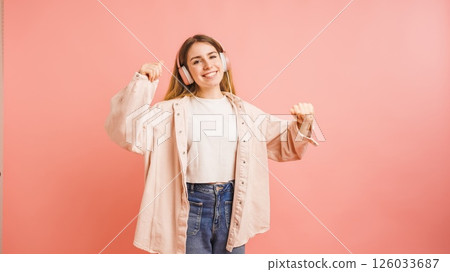 Young woman dancing and listening music with headphones on pink background 126033687