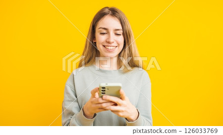 Smiling young woman using smartphone on yellow background Smiling young woman using smartphone on yellow background 126033769