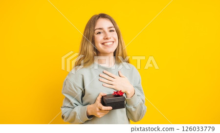 Happy woman holding gift box expressing gratitude on yellow background Happy woman holding gift box expressing gratitude on yellow background 126033779