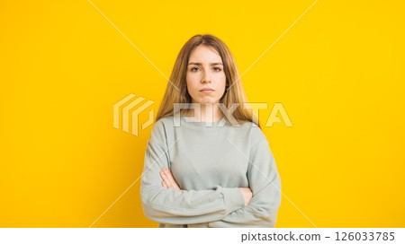Serious young woman crossing arms on yellow background 126033785