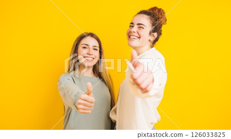 Two happy women showing thumbs up on yellow background Two happy women showing thumbs up on yellow background 126033825