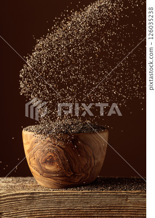 Chia seeds is poured into a wooden bowl. Chia seeds is poured into a wooden bowl. 126035238