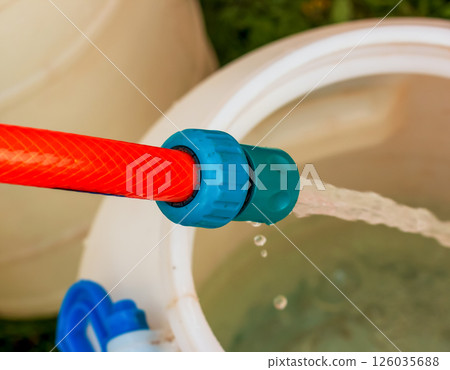 A jet of water from a hose fills a plastic barrel. Background image. The concept of the drinking water crisis in the world. 126035688