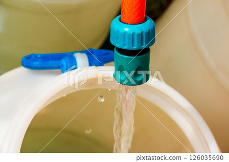 A jet of water from a hose fills a plastic barrel. Background image. The concept of the drinking water crisis in the world. A jet of water from a hose fills a plastic barrel. Background image. The concept of the drinking water crisis in the world. 126035690