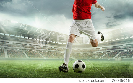 Soccer player in red jersey and white shorts about to strike ball on vibrant green field during outdoor match. 3D stadium. 126036046