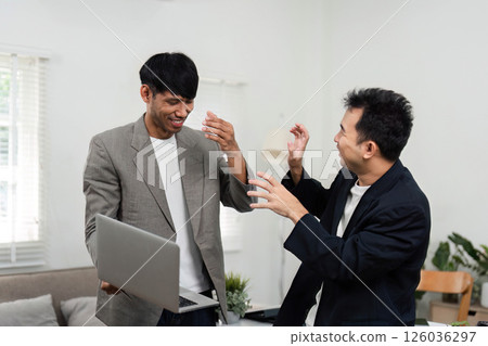 Business Strategy and Team Spirit. Two men celebrating a successful collaboration, reflecting teamwork and positive energy in a modern office. Business Strategy and Team Spirit. Two men celebrating a successful collaboration, reflecting teamwork and positive energy in a modern office. 126036297