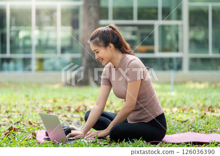 Remote Work and Relaxation. A woman sits on a yoga mat working on her laptop while enjoying nature. Remote Work and Relaxation. A woman sits on a yoga mat working on her laptop while enjoying nature. 126036390