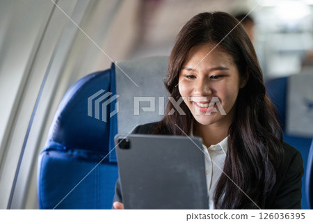 Business travel: Young woman smiling while using a tablet on a flight 126036395