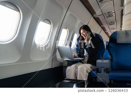 Business travel woman on phone working on laptop in airplane Business travel woman on phone working on laptop in airplane 126036433