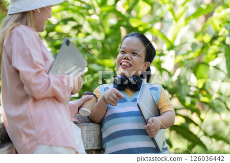 Diverse friends discussing ideas in a sunny park, enjoying their day outside with tablets and headphones 126036442