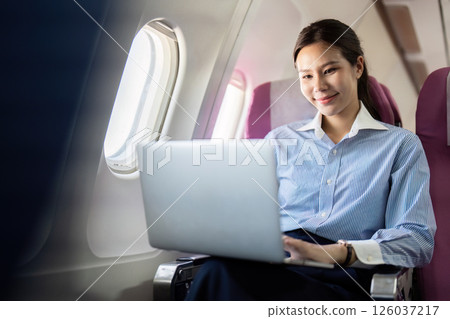 Business travel: Young woman working on laptop and smiling during flight 126037217