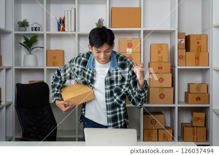 Entrepreneurship and Online Business Success. A young man celebrates a sale in his home office. 126037494