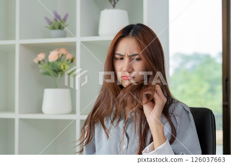 Frustration and Hair Health. A woman examining her damaged hair with concern. Frustration and Hair Health. A woman examining her damaged hair with concern. 126037663