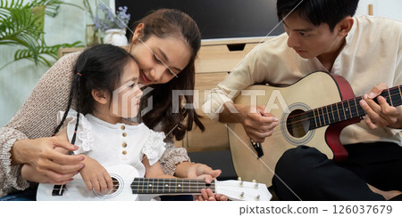 Family and Bonding. A mother and daughter enjoy a music lesson together with a ukulele, fostering their emotional connection. 126037679