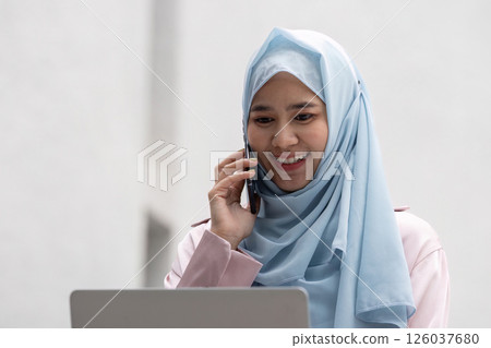 Muslim woman in hijab engaged in business call while using laptop 126037680
